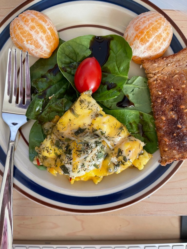 food face: peeled orange halves for eyes, spinach face, omelet for moth, tomato for nose with a side of whole grain toast for an ear on plate with fork