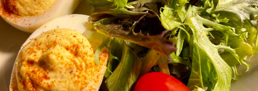 breakfast: deviled eggs, grape tomatoes, arugula on a tan plate with navy band around edge
