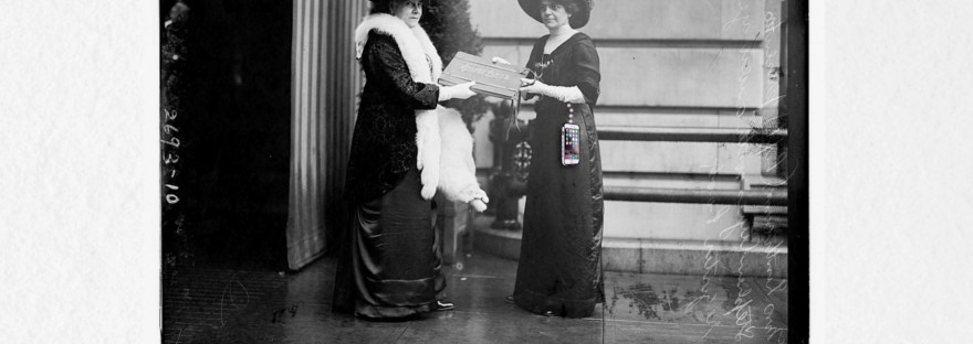 black and white photo of two women, a book between them and an iPhone dangling from the woman on the right with the words below the picture: Don’t Mess with Mrs Ayers! That’s Mrs Helen Ayres of the Woman's National Democratic League (WNDL)— for she holds the registration book. Watch for the ‘Welcome’ email.