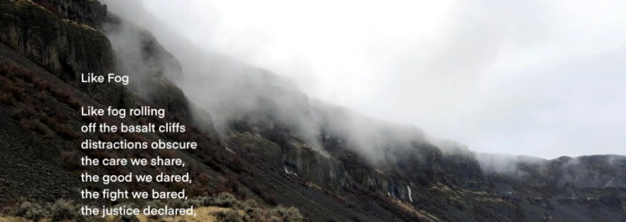 Fog rolls off cliffs of basalt above a highway and grassland.