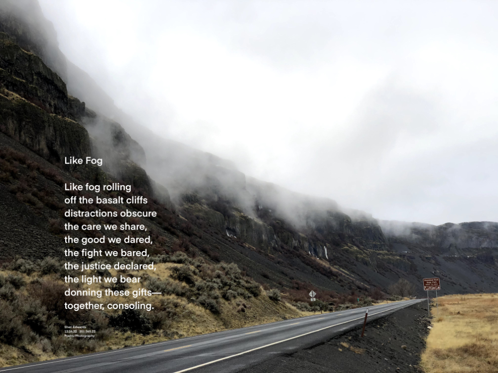 Fog rolls off cliffs of basalt above a highway and grassland.