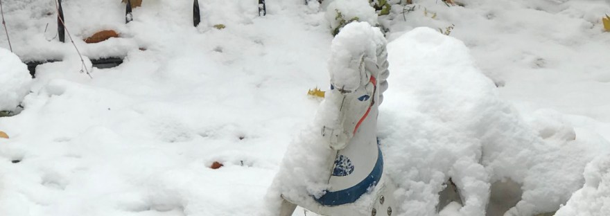 Old toy horse peeking out through freshly fallen snow, abandoned by old fencing with a spattering of yellow autumn leaves