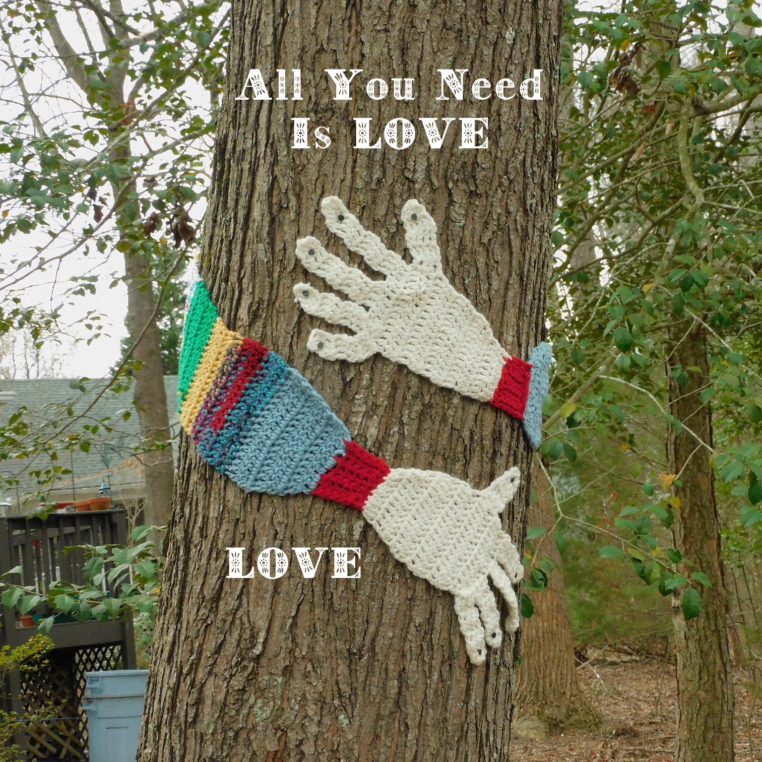 Knitted arms around a tree with added text “Love Is all you need; Love”