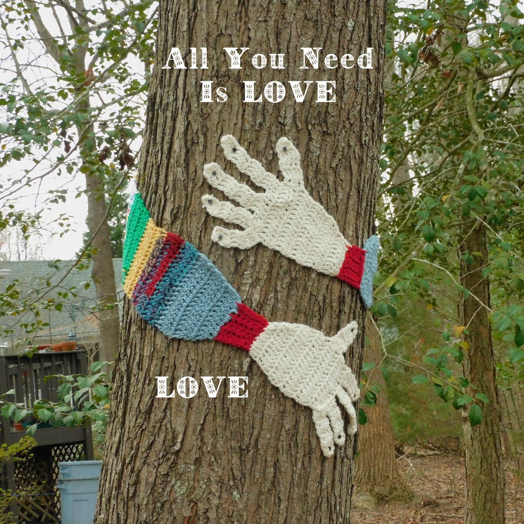 Knitted arms around a tree with added text “Love Is all you need; Love”