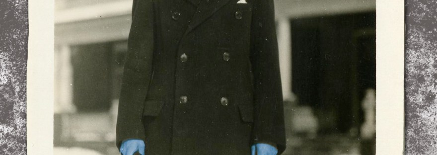 Blue Man in dark hat, dark long coat, and dark sunglasses in front of snowy neighborhood