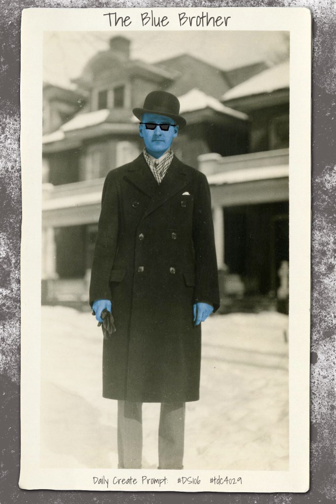 Blue Man in dark hat, dark long coat, and dark sunglasses in front of snowy neighborhood