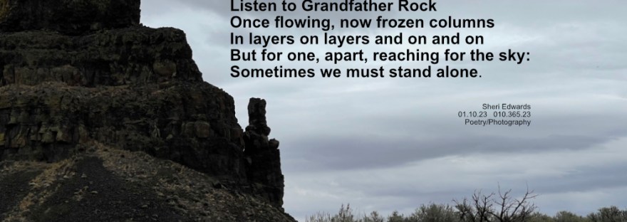 Ancient basalt lava flow in columns with one apart below grey skies and above grassland in the bed of ancient Dry Falls, WA
