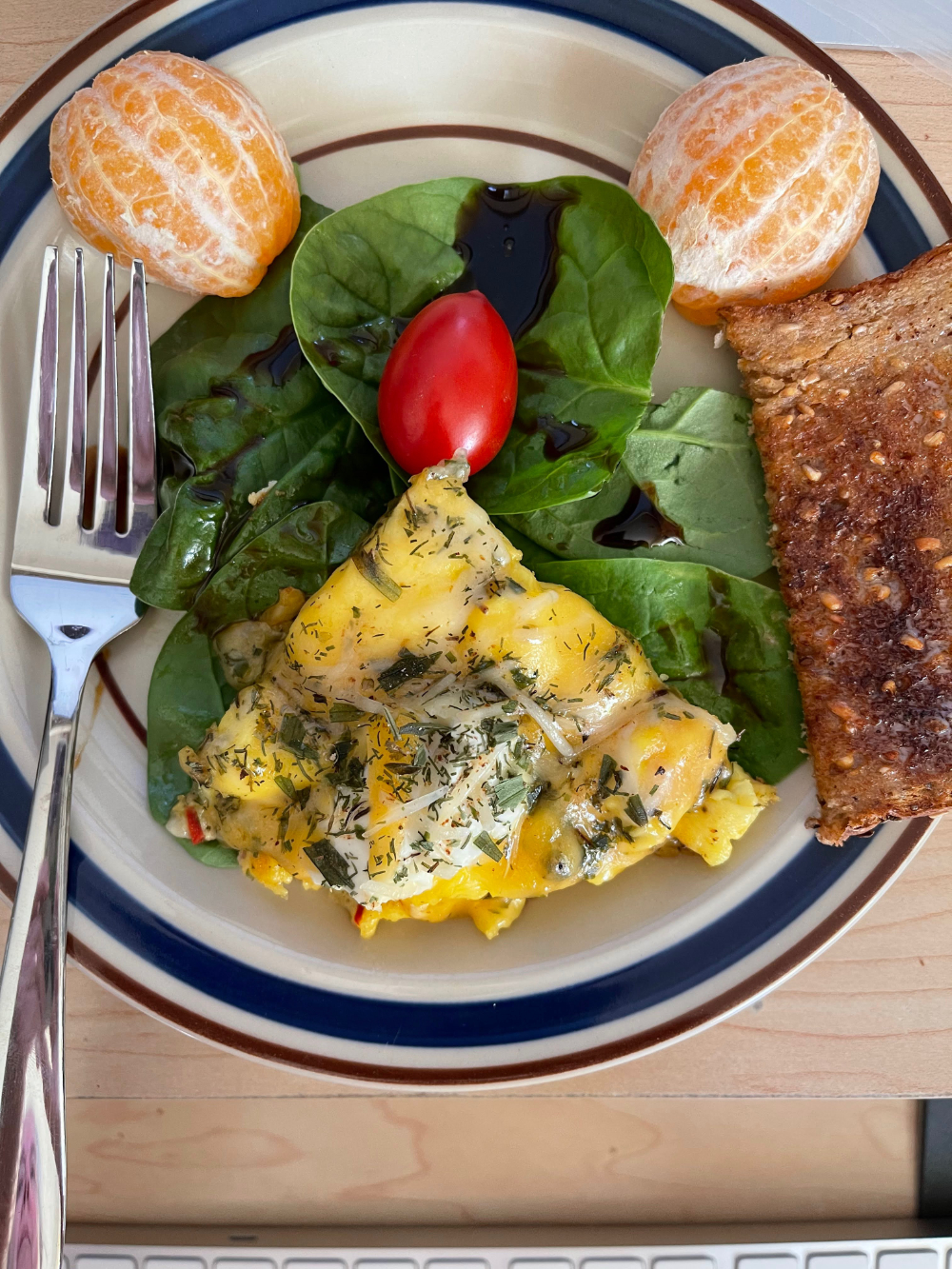 The Face of Breakfast: a triangle egg frittata with a cherry tomato at the tip on a bed of balsam vinegar topped spinach with two oranges at the top left/right edges of the plate and a side of whole grain toast