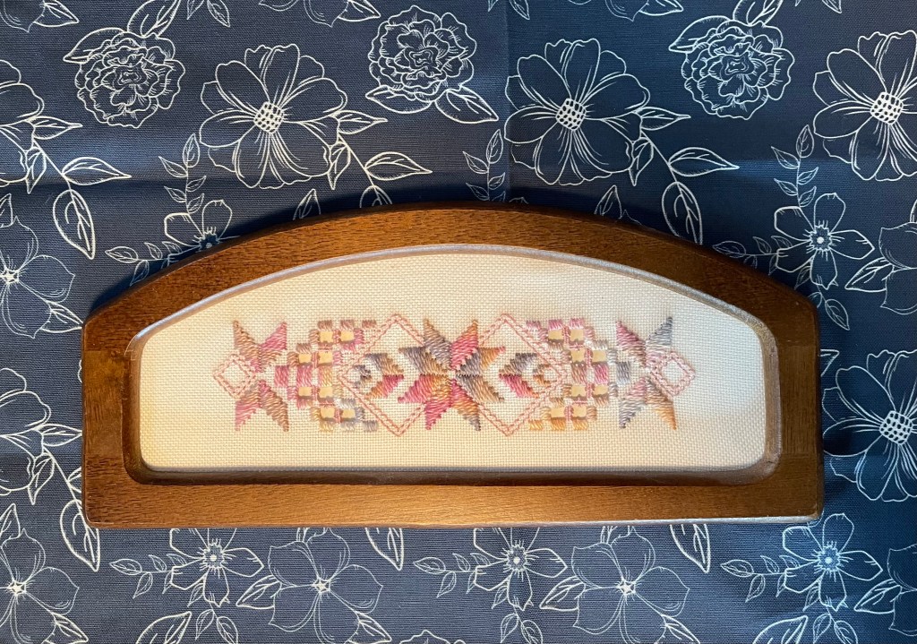 My Aunt Marj’s Hardanger in wooden frame atop my art as placement in white outlined flowers on navy background