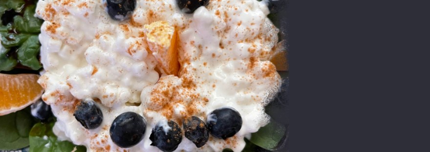 blue flowered plate with a face of orange slices and blueberries in cottage cheese atop a bed of spinach