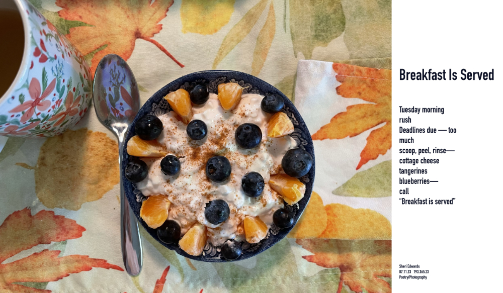 Breakfast of cottage cheese, tangerines, blueberries in.a small blue bowl on placemat of autumn leaves and orange floral coffee cup beside it, reflected in the spoon.
