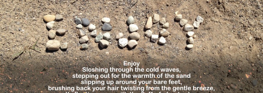 Rocks on the beach arranged into the word, “Enjoy.”