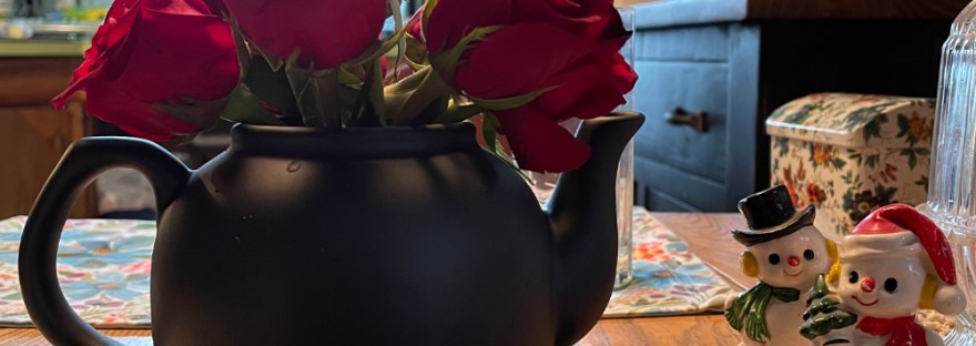 red roses in a black teapot on kitchen table during the holidays