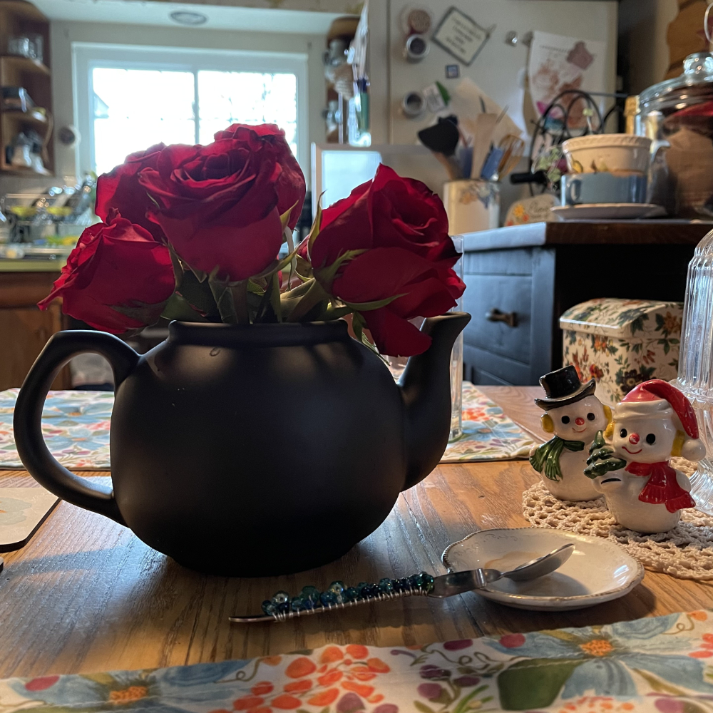 red roses in a black teapot on kitchen table during the holidays