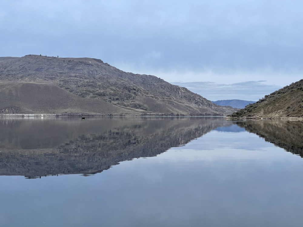 small boat and horizon reflected on Lake Roosevelt on Feb 3rd, 2024, a calm and silent, windless afternoon in the blue-grey hues of sky and lake