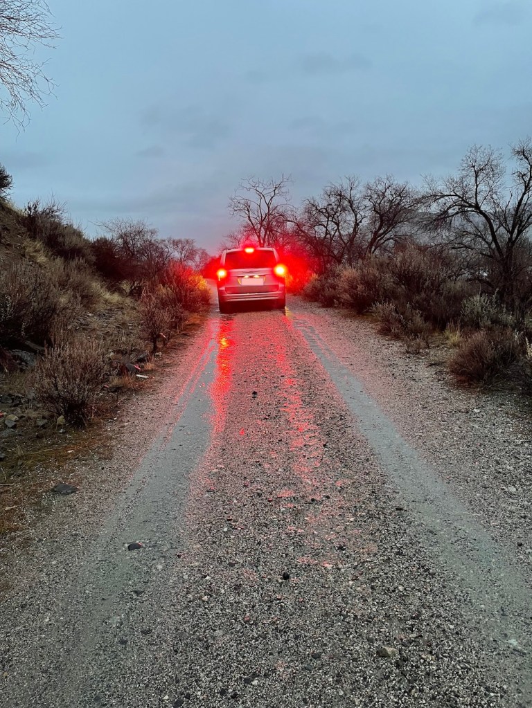 On a usually dusty road, the atmospheric river today began its flooding as seen in the reflection of my car's lights on the running water in the road.