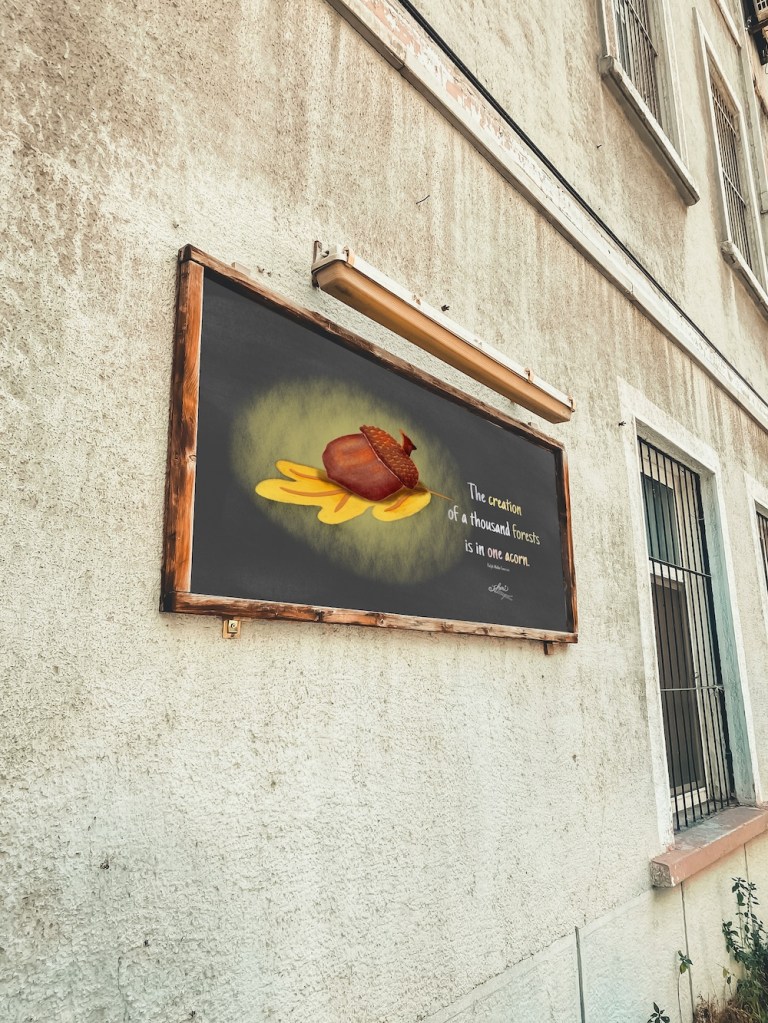 mockup inside chalkboard on building: poster inside frame --acorn on oak leaf with quote "The creation of a thousand forests is in one acorn. Ralph Waldo Emerson; by Sheri42