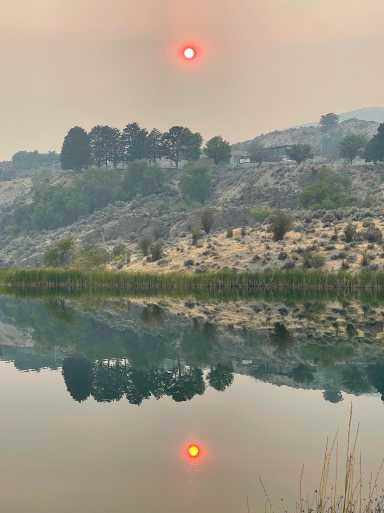 The sun through Washington State wildfire smoke in calm weather, reflecting the landscape at Crescent Lake in Grand Coulee.